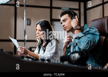 selective focus of concentrated mixed race sound producer in earphones near pretty colleague working at mixing console Stock Photo