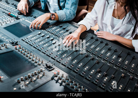 cropped view of two multicultural sound producers working at mixing console in recording studio Stock Photo