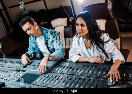 two young attentive multicultural sound producers working at mixing console in recording studio Stock Photo