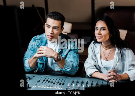 two attentive multicultural sound producers working at mixing console in recording studio Stock Photo