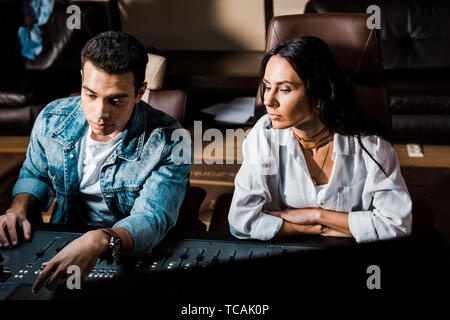 two concentrated multicultural sound producers working at mixing console in recording studio Stock Photo