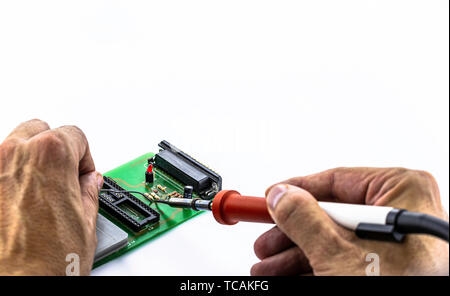 Male hands solder components onto a printed circuit board using tin and a soldering iron. Electronics repair. Selective focus Stock Photo
