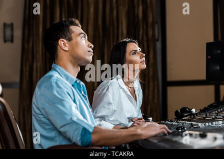 two attentive multicultural colleagues working at mixing console in recording studio Stock Photo