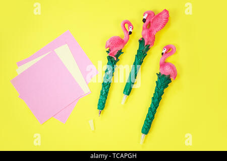 Desktop flatlay: pen with flamingo and pink paper lying vibrant yellow background Stock Photo