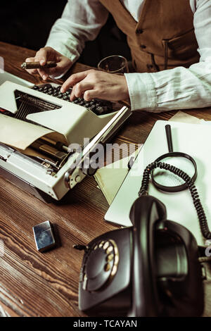Cropped view of detective with cigar using typewriter in dark office Stock Photo