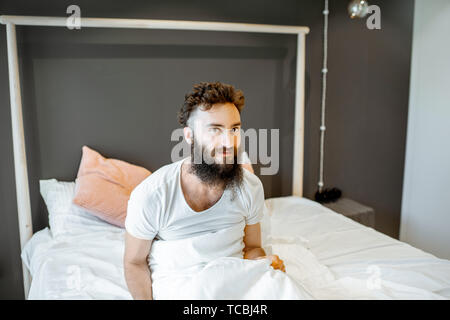 Portrait of enthusiastic bearded man, waking up in the bed, feeling good in the morning Stock Photo