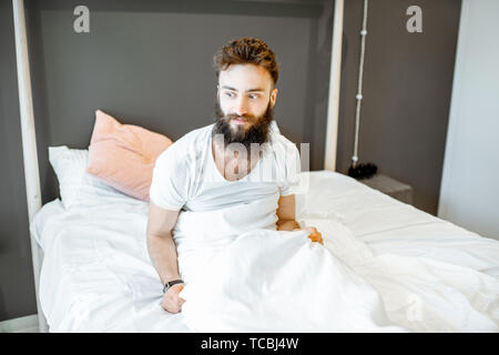Portrait of a bearded man waking up in the bed, feeling frustrated or uncomfortable in the morning Stock Photo
