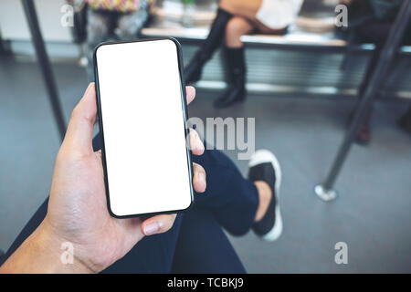 Mockup image of hand holding white mobile phone with blank black screen in subway Stock Photo