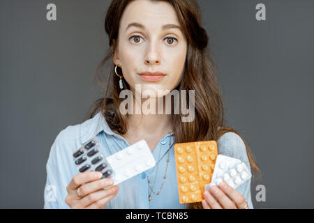 Portrait of a young and sad woman holding different medicines on the grey background