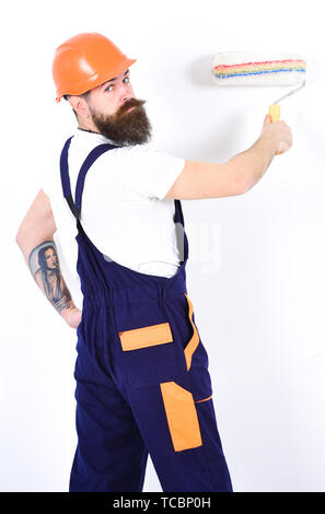 Apartment redecoration. Turn back painter with paint roller in front of white wall. Bearded man with tattoo on his arm isolated on white background. Stock Photo