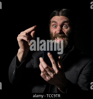 Old believer senior priest with a smartphone, bearded old man is calling on a dark background Stock Photo