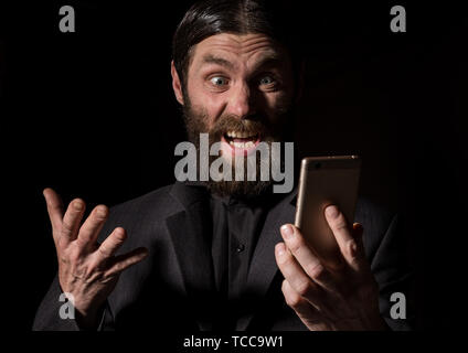 Old believer senior priest with a smartphone, bearded old man is calling on a dark background Stock Photo