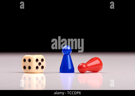 Standing blue playing figurine as winner and lying red figurine as loser with playing dice on white table top with black background. Space for your te Stock Photo