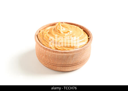 Creamy peanut butter in wooden bowl isolated on white background. A traditional product of American cuisine Stock Photo