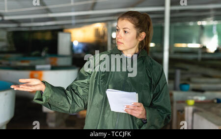 Female fish farm worker checking trout growth in fish breeding incubator Stock Photo