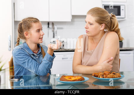 Attractive mother and her teenage daughter having conversation at kitchen table Stock Photo