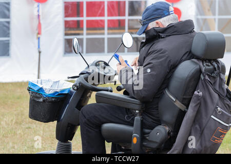 A middle aged man on a mobility scooter using his mobile phone or cell phone Stock Photo