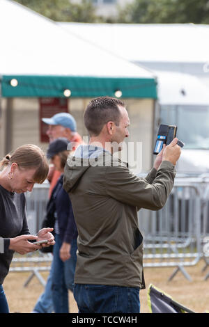 A man using a mobile phone or cell phone to take a photo at an outdoor event Stock Photo