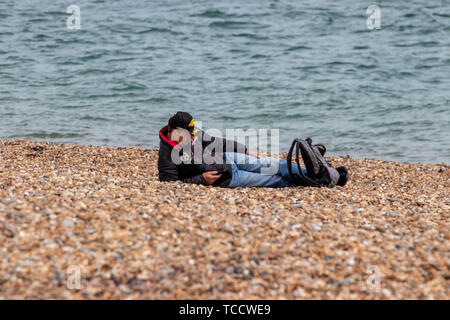 A man laying on a pebble beach using his mobile phone or cell phone Stock Photo