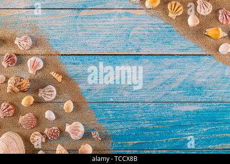 Summer time concept with sea shells on a blue wooden background and sand. Seashells frame on wooden background nautical border. Focus on seashells.
