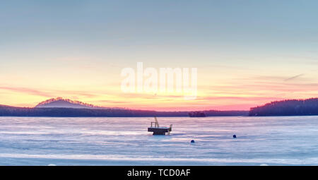 Summer resort under ice within long winter.  Breathtaking sunset with golden and pink clouds over frozen lake Stock Photo