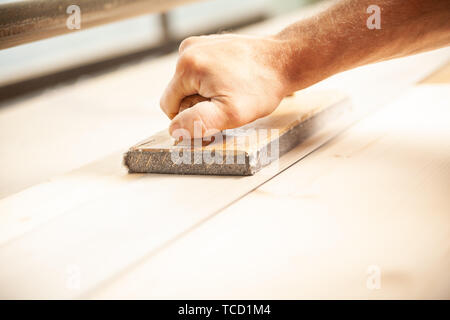 Woodworker using sander tool with handle to smooth down long plank of wood. Motion blur on moving sander tool. Stock Photo