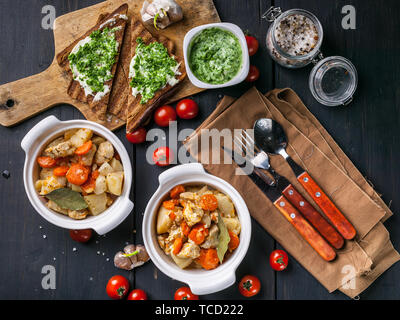 Two bowls of chicken baked with potatoes and carrots, sandwich with cheese and cherry tomatoes on a dark wooden background. Top view Stock Photo