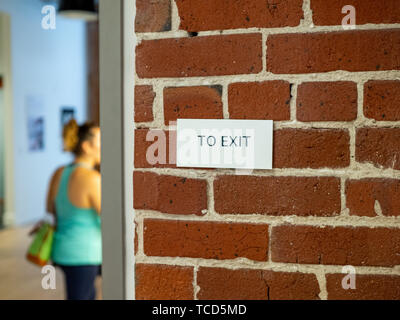 Woman in athletic clothes with in direction of exit sign on brick wall Stock Photo