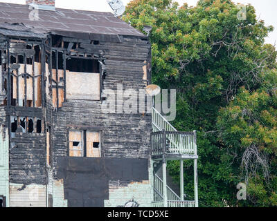 Large, old dilapidated house with boarded up windows, rusted equipment next to tree Stock Photo