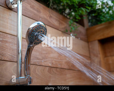 Water steams flowing out of handheld shower head in outdoor shower Stock Photo