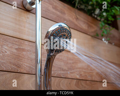 Waterjets flowing out of handheld shower head in outdoor shower Stock Photo
