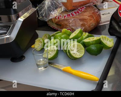 Squeezed lime, shot glass and knife sitting on small cutting board, making margaritas for party Stock Photo