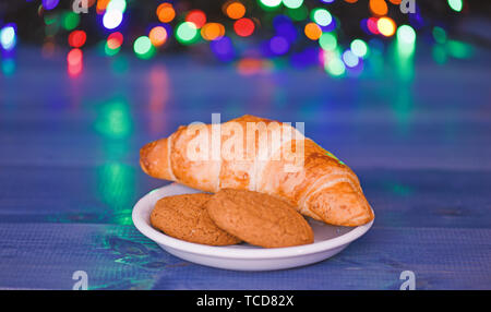 What do kids around world leave for Santa. Croissant and oat cookies on white plate. Winter holiday tradition. Sweets for Santa Claus and his helpers. Santa treats recipe. Treats for Santa concept. Stock Photo