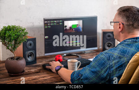 Businessman or photographer editing photographs on a large desk top monitor in an office in an over the shoulder view onto his desk Stock Photo