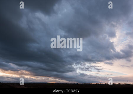 From below view of dark thick thunderclouds with vast green field under Stock Photo