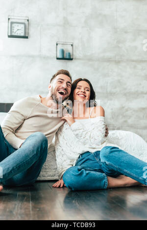 low angle view of happy man and woman sitting on floor and watching movie at home