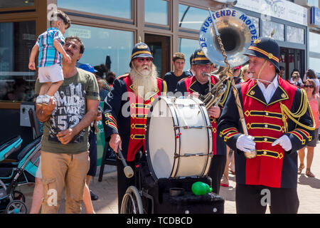 Funny Belgian three man marching band / fanfare band / brass band De Rustende Moeders playing the sousaphone and bass drum on the street in Belgium Stock Photo