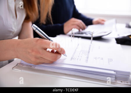 Close-up Businesswoman's Hand Checking Invoice Over Desk In Office Stock Photo