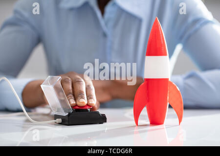 Businesswoman's Hand Launching Rocket By Pressing Red Button Stock Photo