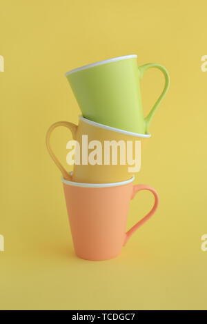 Three colorful yellow and light green and light red ceramic cups on yellow background. Stock Photo