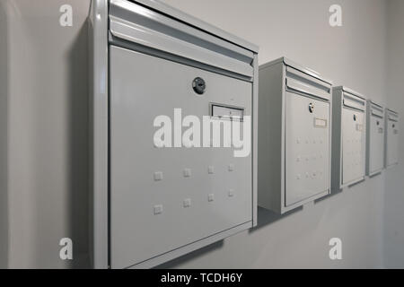 Modern white metallic mail boxes for an apartment in a row against a white painted wall with numbers on them and locks. Stock Photo