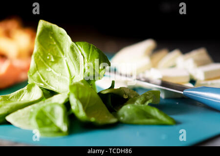 Chopped up ingredients for pizza toppings are laid out on a bright blue chopping board - Includes Basil, Ham, Cheese and mushroom Stock Photo