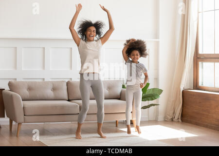 African mom with kid girl jumping dancing in living room