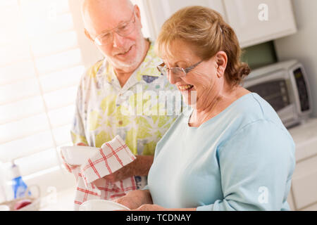 Senior Adult Couple Having Fun Washing Dishes Together Inside Kitchen of Their House. Stock Photo