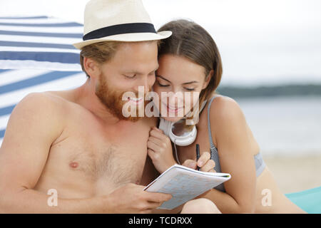couple on the beach doing crosswords Stock Photo