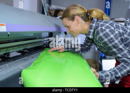 female worker inserting shiny green paper in machine Stock Photo