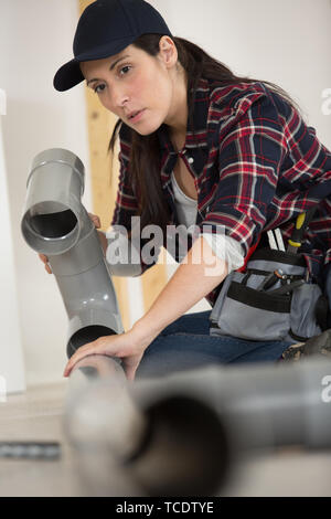 woman in dungarees carrying plastic pipes Stock Photo
