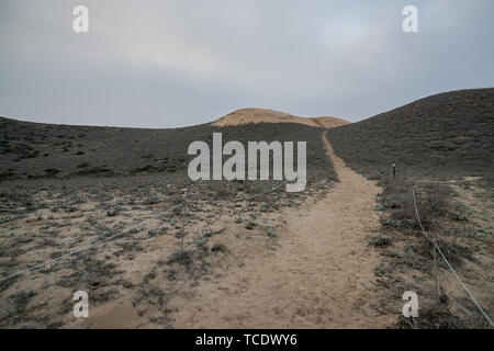View to sandy path leading to small hills in cloudy day Stock Photo