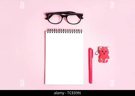 Notepad with trendy glasses and pink coral pen and toy bear gift on pastel pink background. Stock Photo