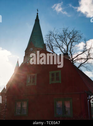 Typical wooden residential house painted in traditional falun red in the cultural preserve of Vita Bergen and the spire of Sofia Church, Stockholm Stock Photo